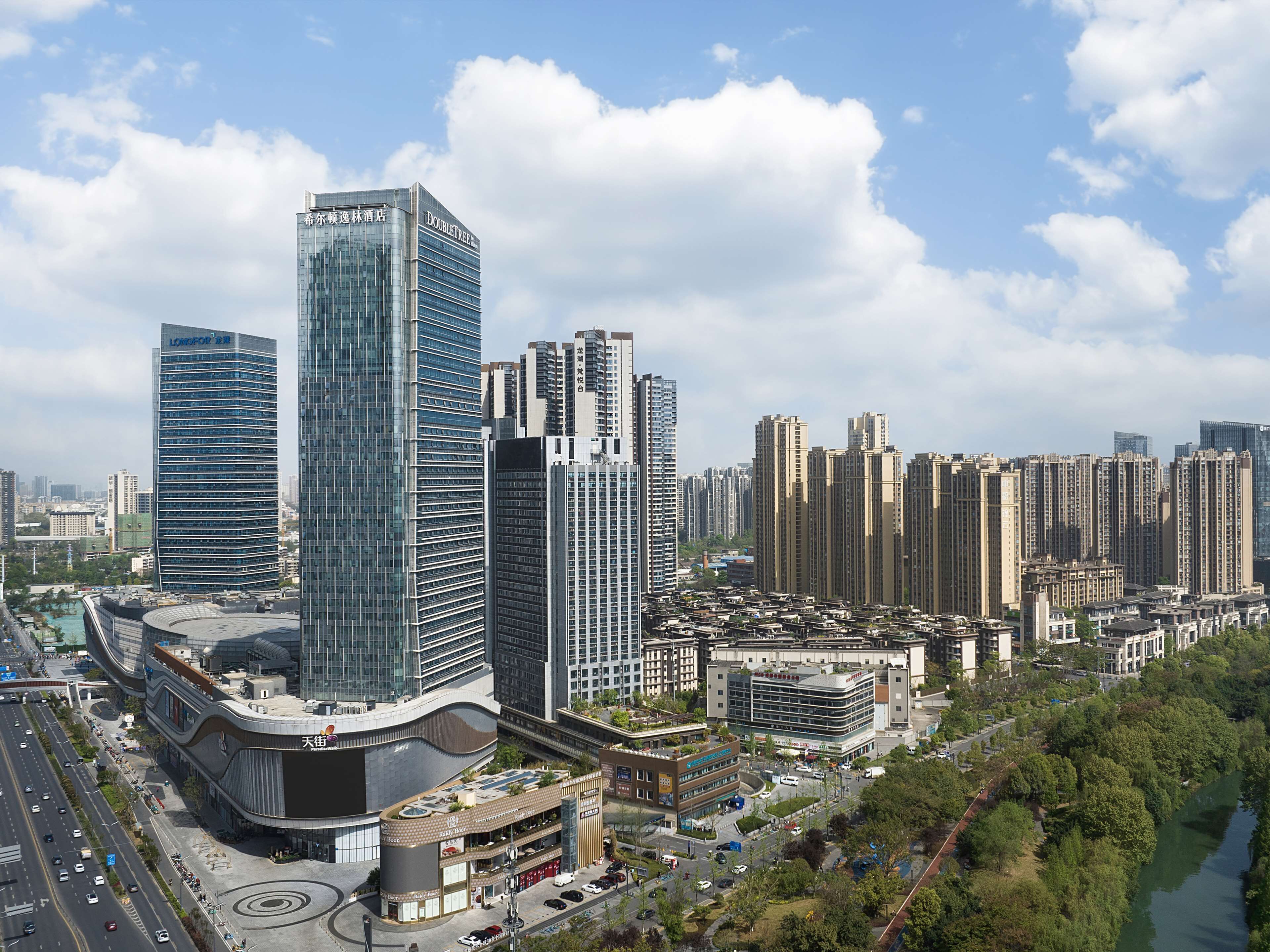 A high-rise hotel with a modern glass facade, surrounded by other tall buildings and a river.