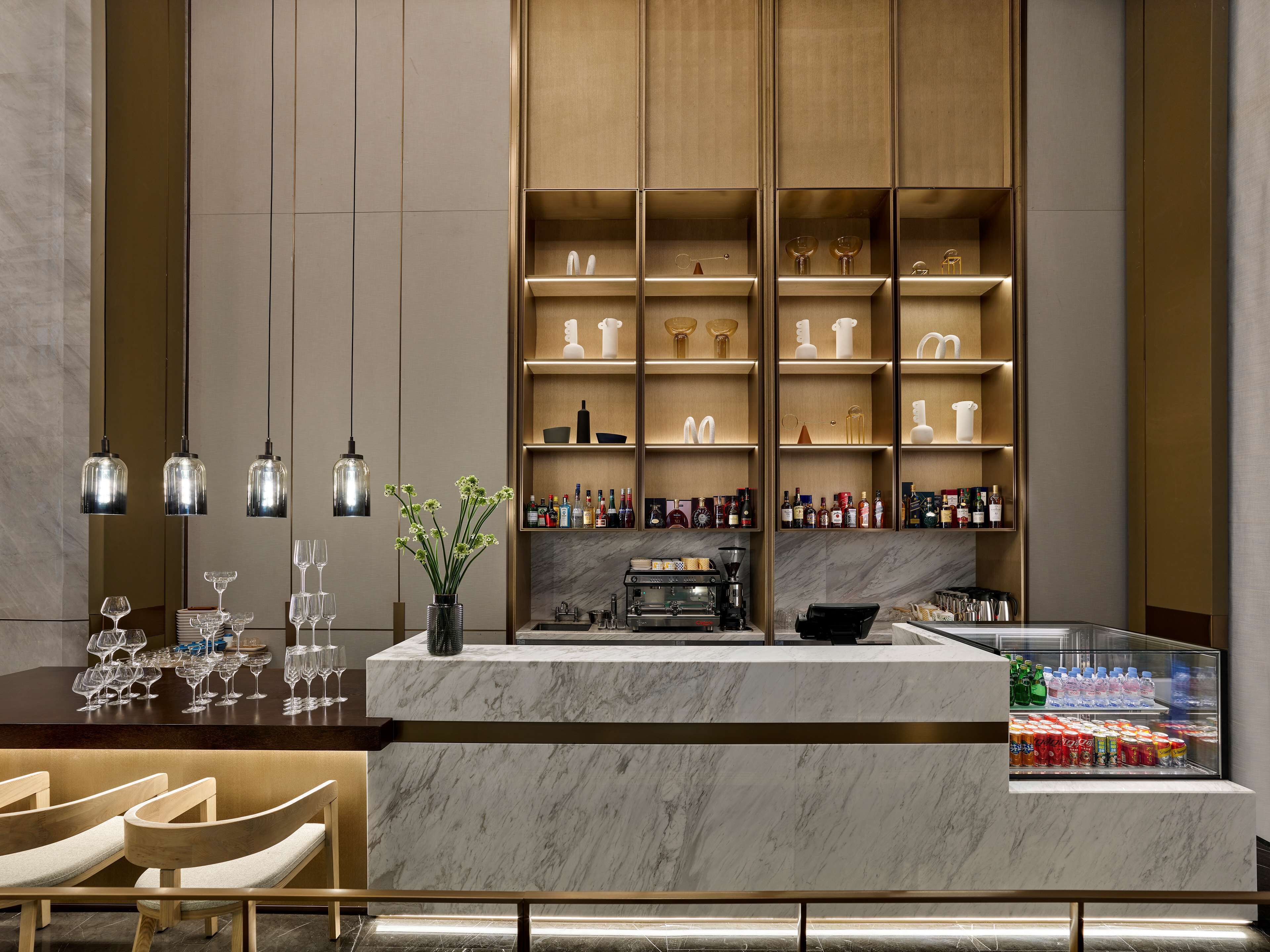 Uma área de bar moderna com bancadas de mármore, uma máquina de café e prateleiras com garrafas e copos.