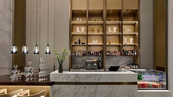 A modern bar area with marble countertops, a coffee machine, and shelves with bottles and glasses.