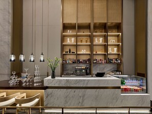 A modern bar area with marble countertops, a coffee machine, and shelves with bottles and glasses.