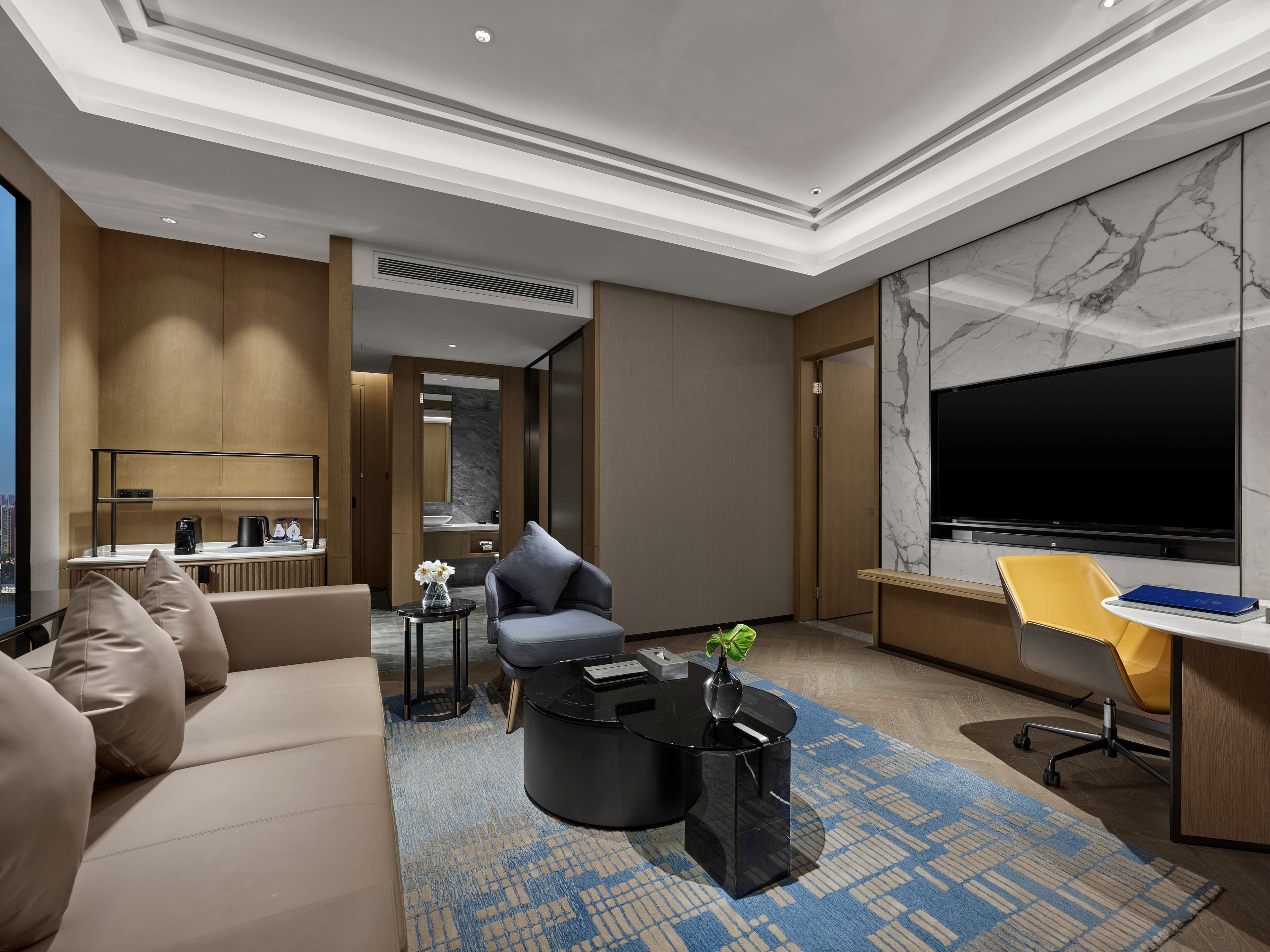 A modern hotel room with a sofa, a coffee table, a TV, and a desk.