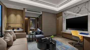 A modern hotel room with a sofa, a coffee table, a TV, and a desk.