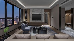 Un salón moderno con un televisor grande, asientos cómodos, una mesa de centro y vistas a la ciudad.