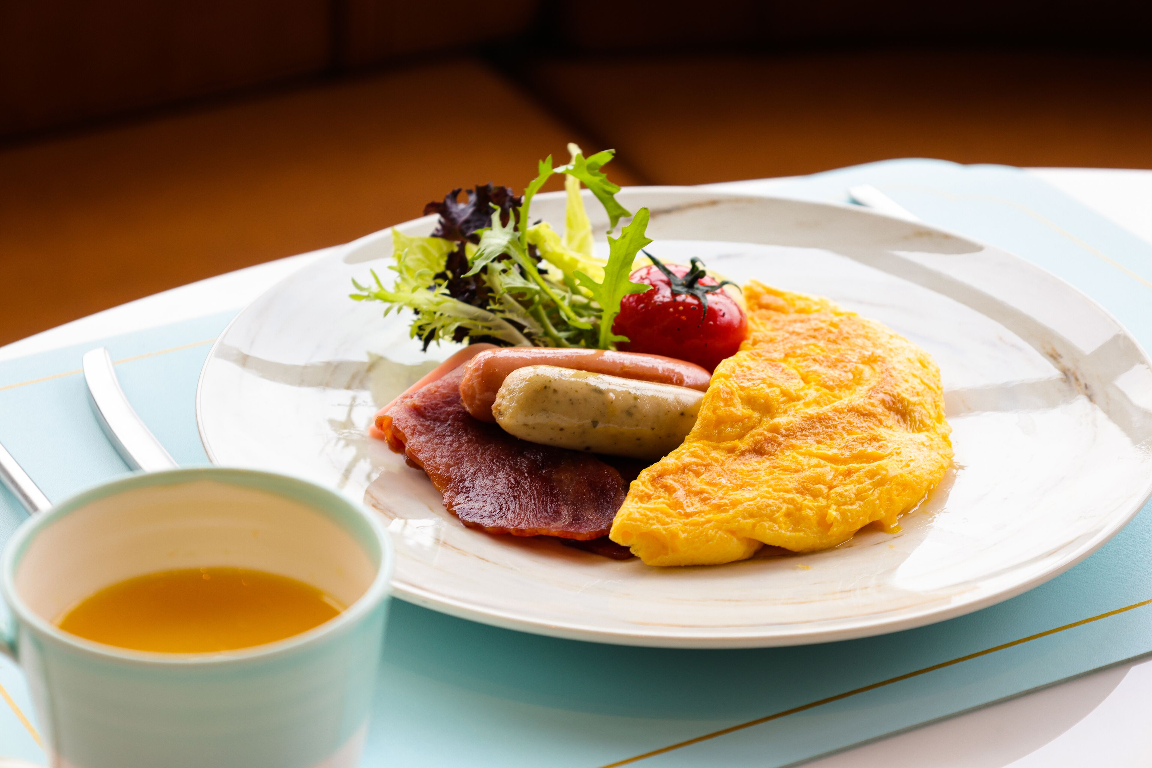 A plate with eggs, bacon, a tomato, and a salad on a table with a cup of tea.