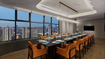 A conference room with a city view, large windows, and a modern chandelier.