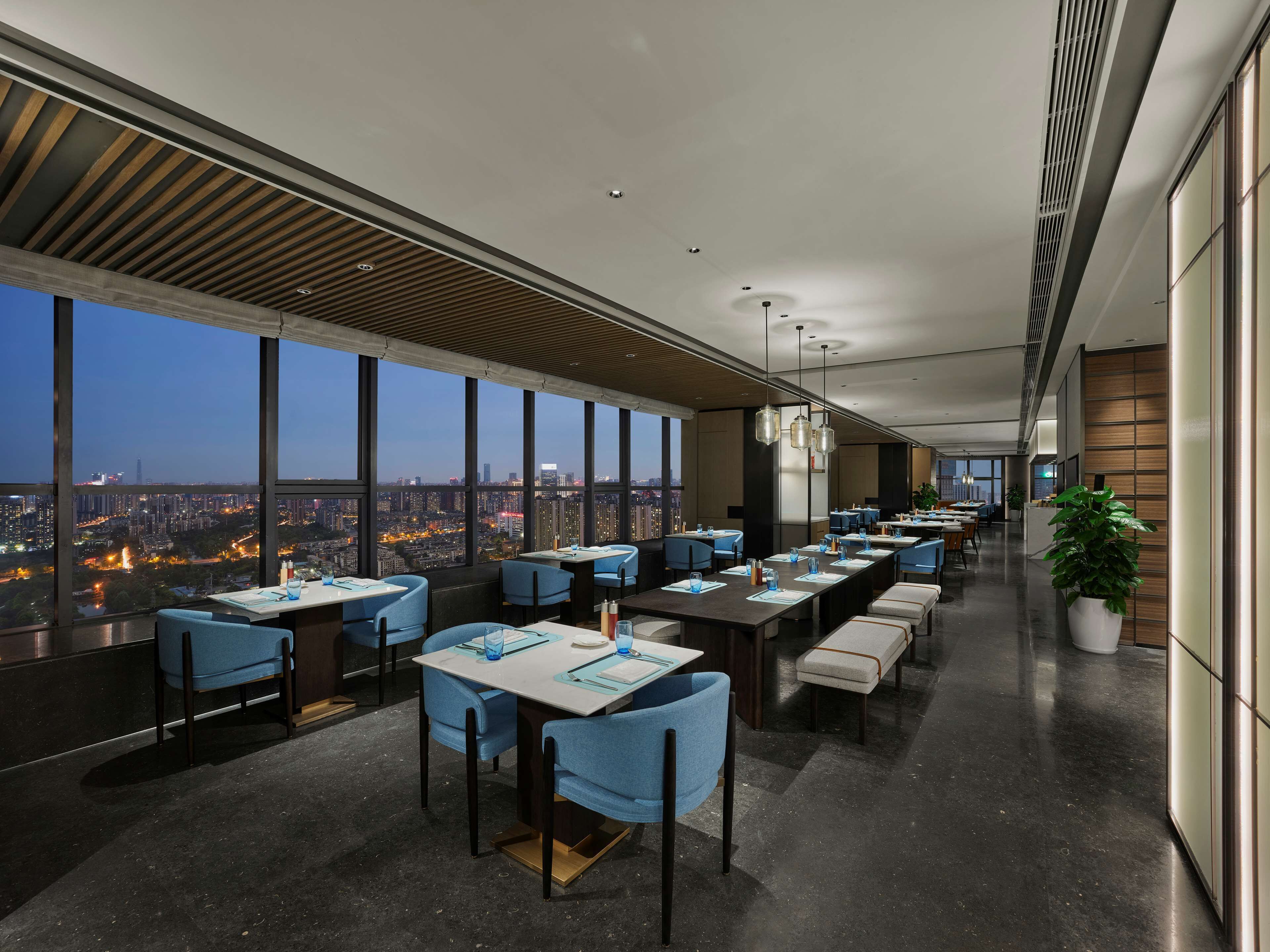 Un espace de restauration moderne doté de hauts plafonds, de grandes fenêtres offrant une vue sur la ville et de meubles contemporains.