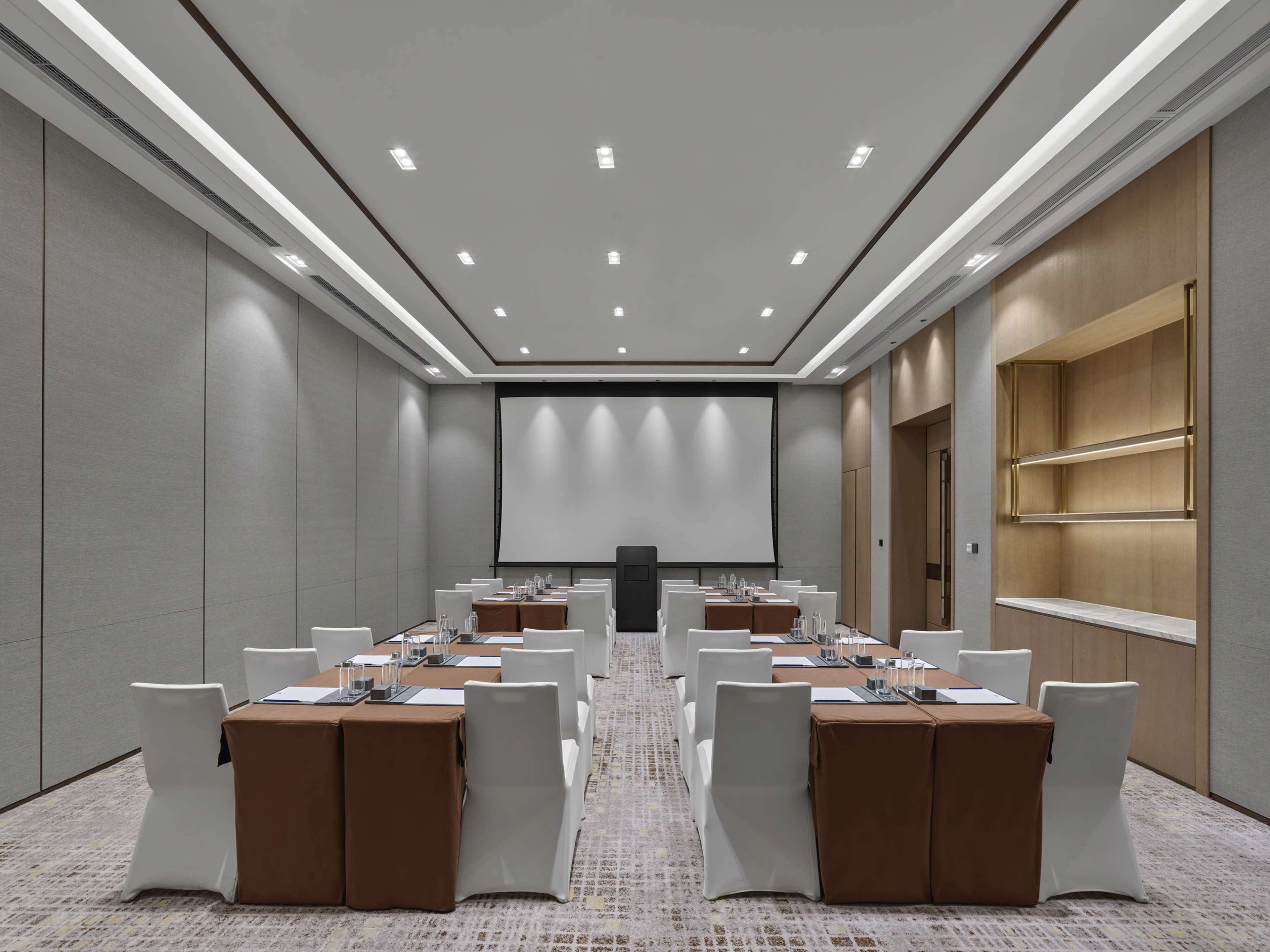 A conference room with a long table, white chairs, and a projector screen.