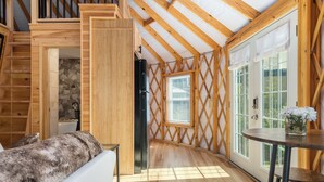 Un interior de madera con una escalera, un refrigerador, una mesa de comedor y un ventanal con persianas.