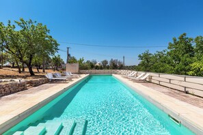 A rectangular swimming pool with clear blue water, surrounded by a stone deck and shaded by trees. - Villa Sessana by Perle di Puglia (Ostuni)