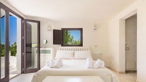 A bedroom with a bed, a window, a bathroom, and a door leading to an outdoor area.