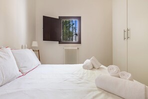 Een slaapkamer met een bed, een raam, een radiator en een kledingkast.