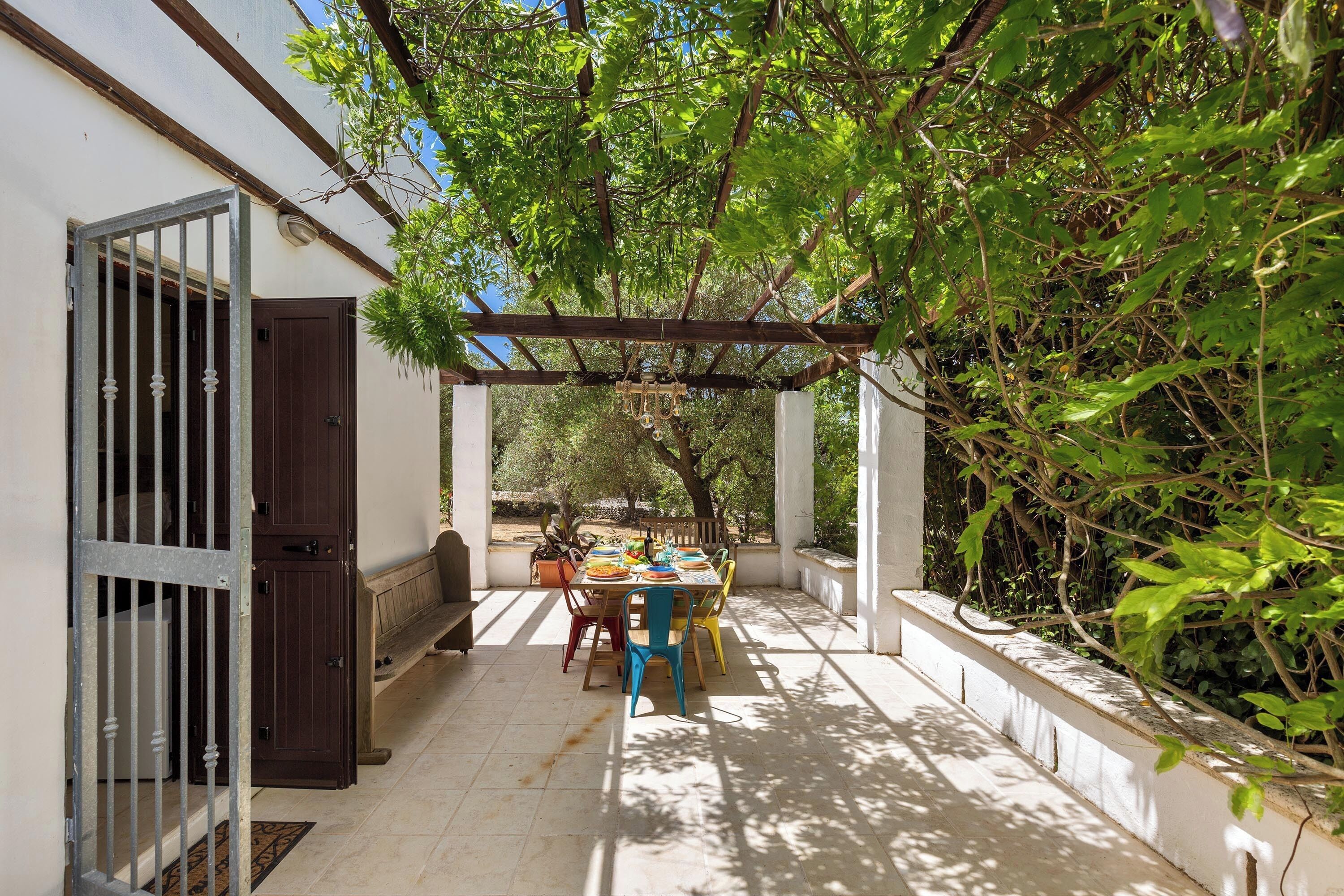 Eine Terrasse im Freien mit Esstisch, umgeben von Pflanzen und einer Pergola.