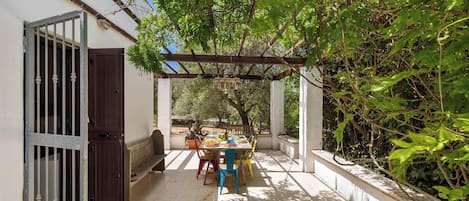 An outdoor patio with a table set for dining, surrounded by greenery and a pergola structure.