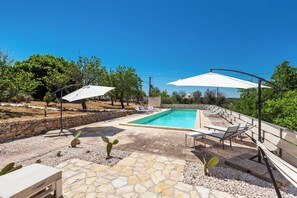 En swimmingpool med en stenbelagt terrasse, omgivet af liggestole og parasoller.