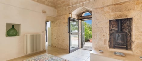 A room with a stone wall, a radiator, a wooden table with patterned tiles, and a fireplace.