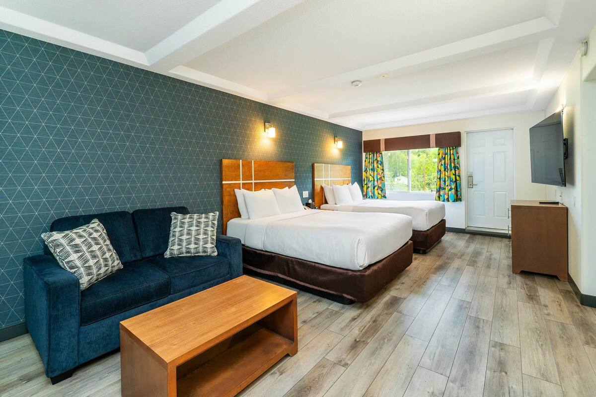 Une chambre d’hôtel avec un canapé bleu, deux lits, une table basse en bois et un téléviseur fixé au mur.