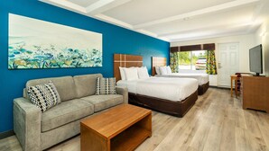 A hotel room with a blue accent wall, a large painting, a sofa, a bed, a wooden coffee table, and a TV. - Quality Inn & Suites (Clearwater)
