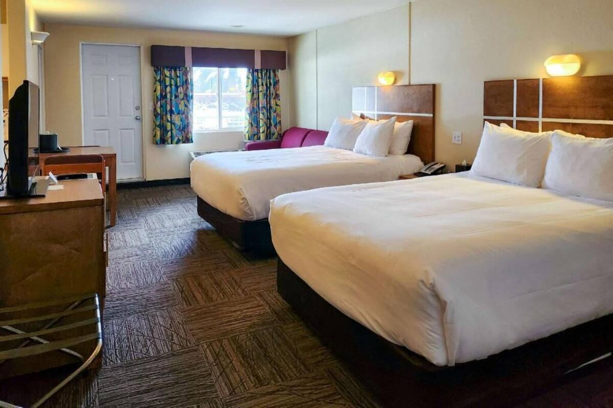 Une chambre d’hôtel avec deux lits, un bureau, une télévision et une fenêtre avec des rideaux.