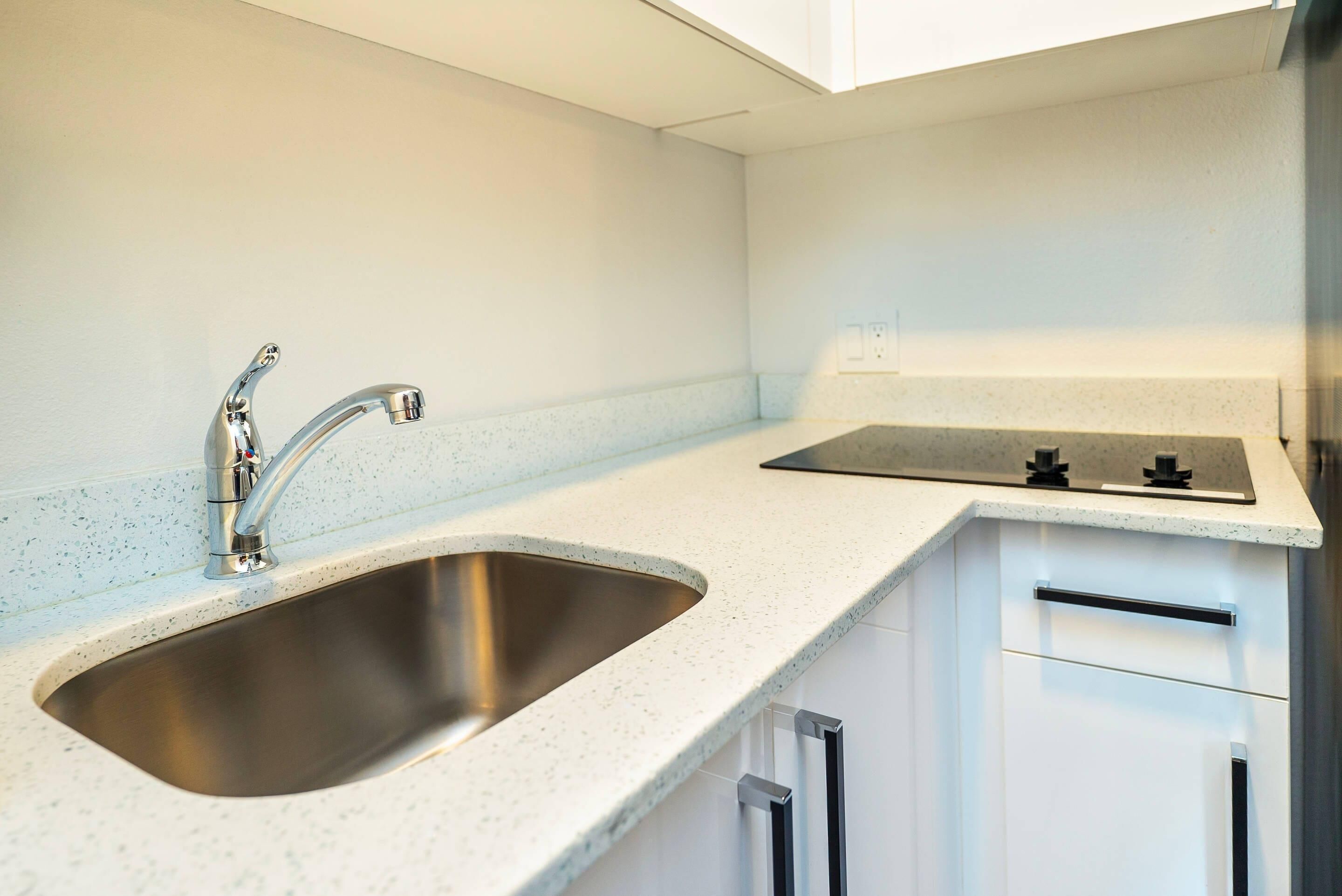 A modern kitchen with a stainless steel sink, a gas stove, and white cabinetry.