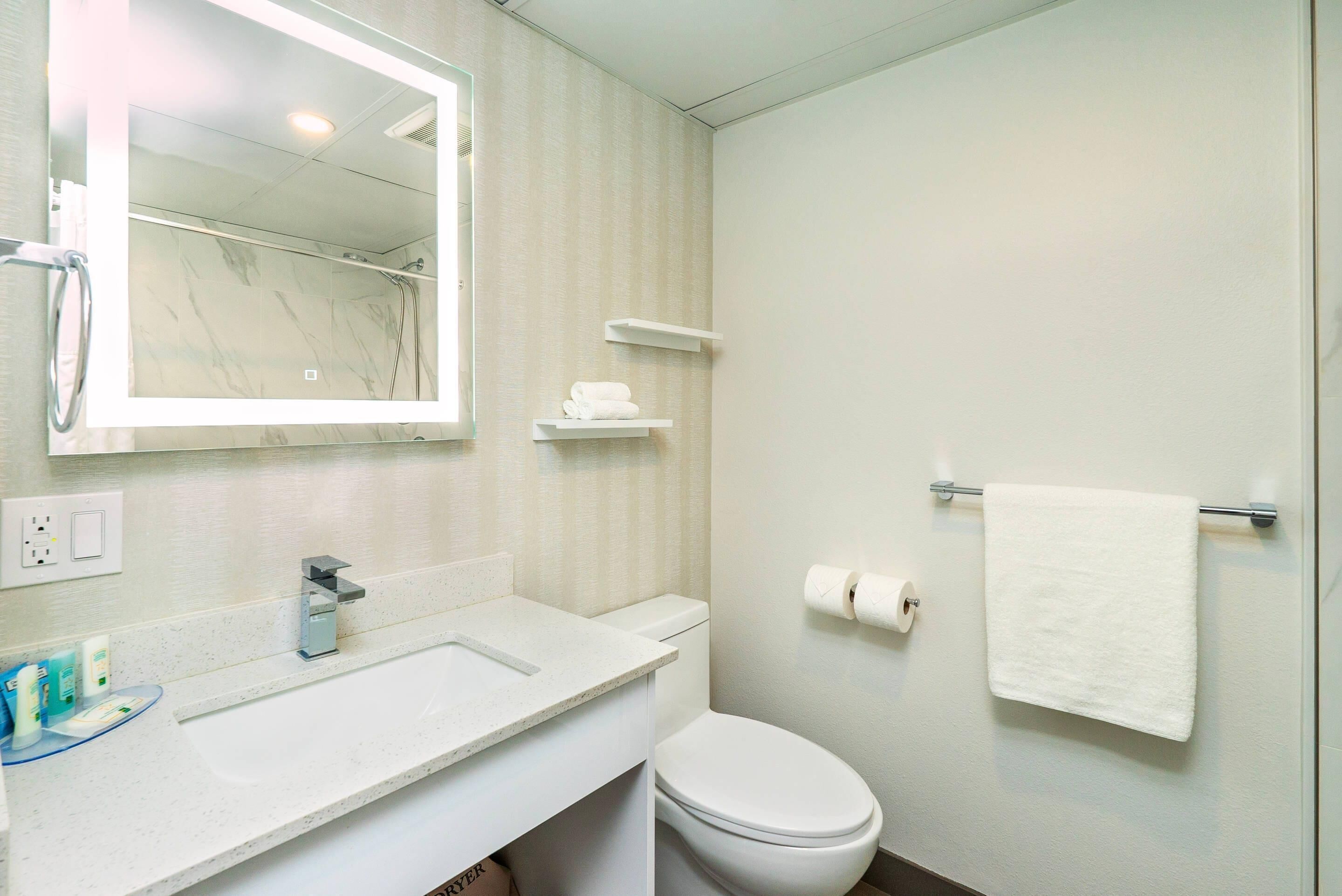 Un baño con un lavamanos blanco, un inodoro, una toalla colgada en la pared y un espejo sobre el lavamanos.
