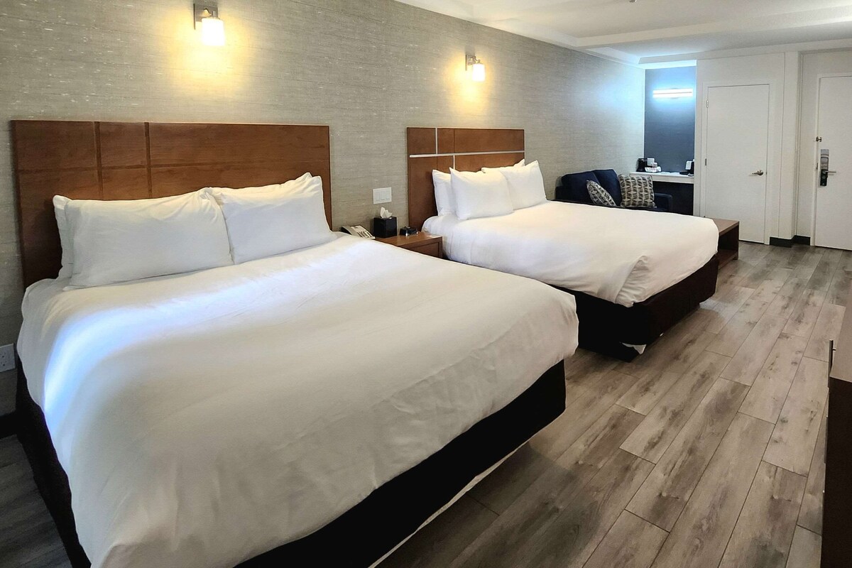 A hotel room with two beds, a desk, a chair, and a bathroom door.