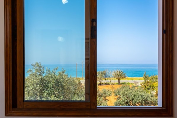 Blick durch ein Holzfenster auf eine Küstenlandschaft mit Bäumen und blauem Himmel.