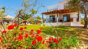 Una casa moderna de dos pisos con balcón, rodeada por un jardín bien cuidado con flores rojas.