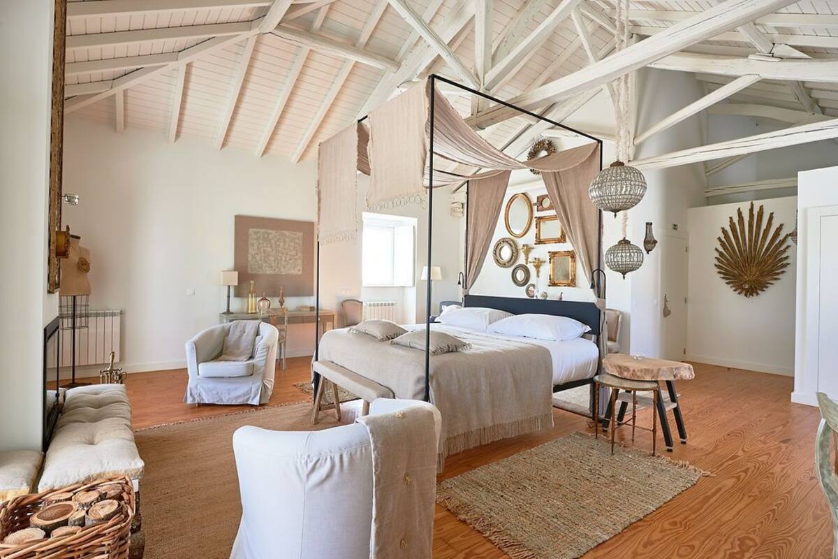A spacious bedroom with a large bed, a sitting area with a chair and bench, and a wooden floor.