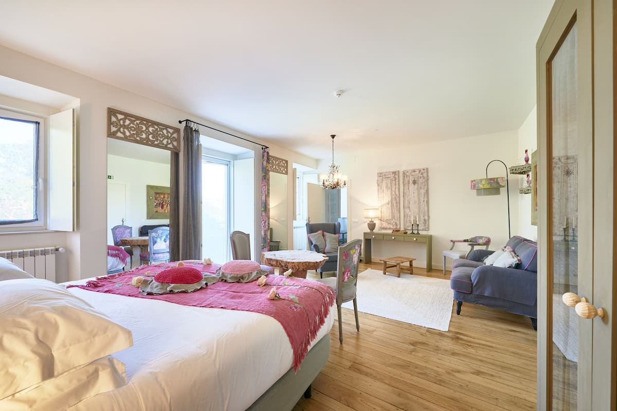 A bedroom with a large bed, a chair, a small table, and a sofa.