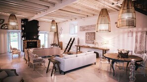 Un salón amplio con un sofá blanco, muebles de madera y una chimenea. Hay lámparas colgantes y vistas al exterior.