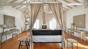 Un dormitorio con cama con dosel, suelo de madera, un escritorio y una silla.