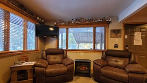 A cozy living room with two leather armchairs, a small wooden side table, a fireplace, and a window with blinds. - Family Adventure Cabin/Near Yellowstone/Hot Tub (Island Park)