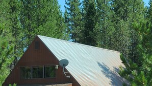 A large wooden cabin with a metal roof, surrounded by dense forest. - Family Adventure Cabin/Near Yellowstone/Hot Tub (Island Park)