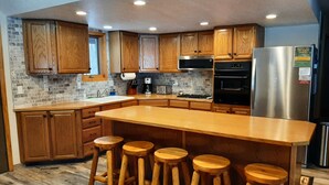 A kitchen with wooden cabinets, a stainless steel refrigerator, a large island with stools, and a brick backsplash. - Family Adventure Cabin/Near Yellowstone/Hot Tub (Island Park)