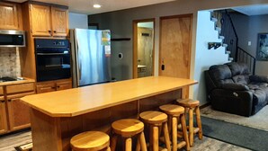 A kitchen with wooden cabinets, a stainless steel refrigerator, a built-in oven, and a wooden bar with stools. - Family Adventure Cabin/Near Yellowstone/Hot Tub (Island Park)