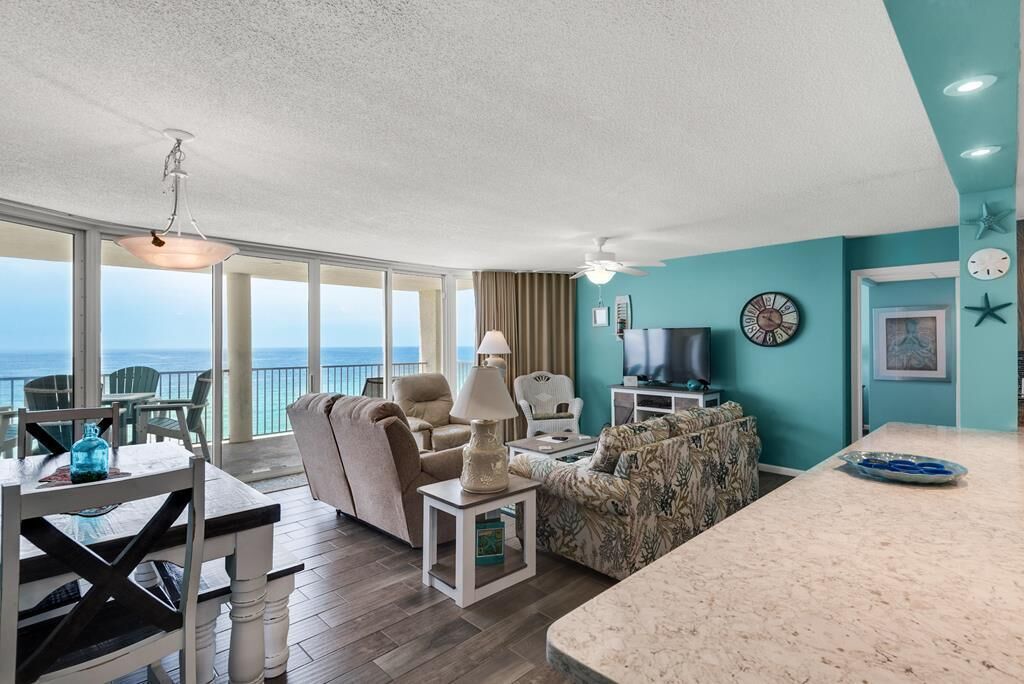 A spacious living area with a large window overlooking the ocean, a comfortable seating arrangement, a television, and a kitchen area.