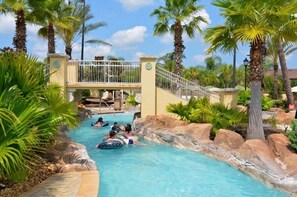 Un espace piscine doté d’un toboggan, de palmiers et d’un pont.
