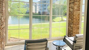 A room with large windows offering a view of a lake and buildings. There are two chairs and a small table. - Astonishing view great condo at Myrtlewood Villas (Myrtle Beach)