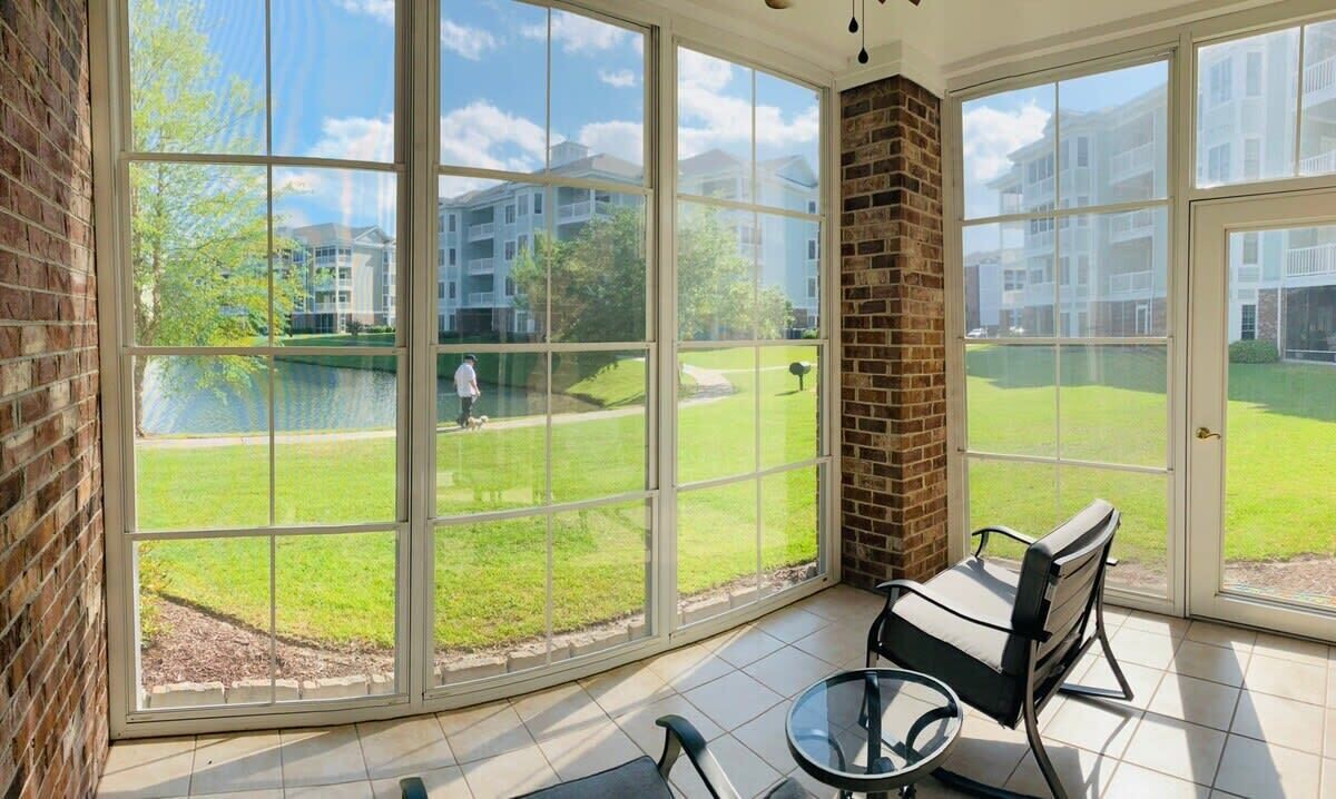A sunlit room with large windows, a brick column, and a view of a golf course and buildings.
