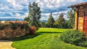 Un jardín bien cuidado con un muro de piedra, una maceta de terracota grande y un edificio rojo con fachada de ladrillo.