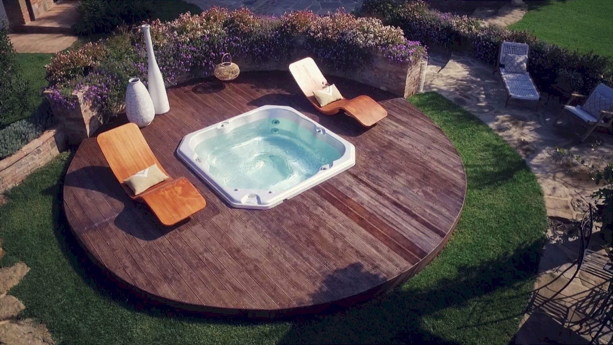 A hot tub surrounded by wooden lounge chairs and planters with flowers.
