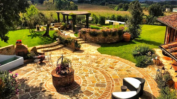 Un patio de piedra con mobiliario exterior, un hogar para fuego y una pérgola.