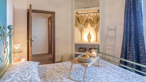 Un dormitorio con cama, mesita de noche, lámpara y estante con objetos decorativos.