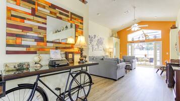 A modern living room with a wooden wall art, a desk with a typewriter, a bicycle, and a grey sofa.