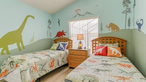 Ein Kinderzimmer mit zwei Betten, Bettwäsche mit Dinosaurier-Motiv und Wandbildern von Dinosauriern und Natur.