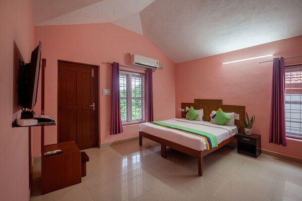 A bedroom with a bed, bedside table, nightstand, TV, and a window with curtains. - Treebo Yajna Comforts (Madikeri)