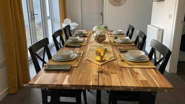 A dining room with a wooden table set for six, surrounded by black chairs.