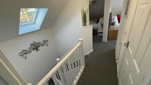 A narrow hallway with a white railing, a small skylight, and a decorative metal piece on the wall.
