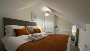 A bedroom with a bed, pillows, a blanket, a door, a radiator, and a hanging light fixture.