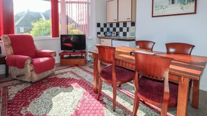Una sala de estar con un sillón rojo, un televisor, una mesa de comedor con sillas, y una zona de cocina con armarios y un salpicadero a cuadros.